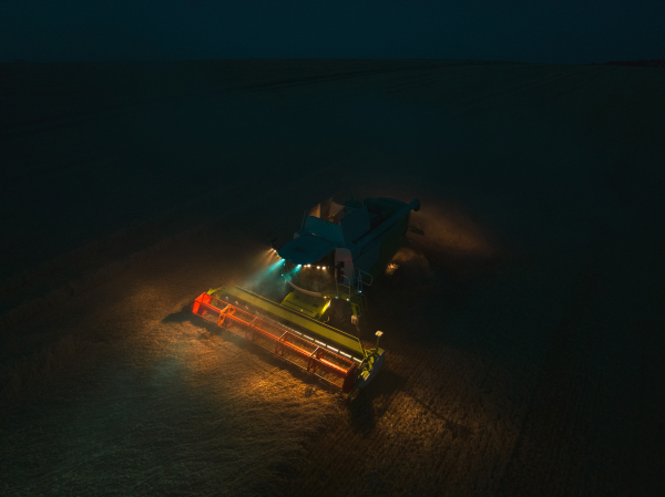 Aerial view of a tractor a harvester working on field during night. Agriculture and cultivation of industrial farms. Agribusiness.