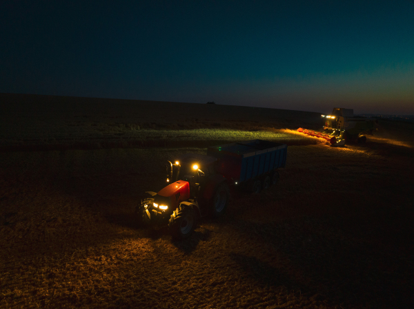 Aerial view of a tractor a harvester working on field during night. Agriculture and cultivation of industrial farms. Agribusiness.