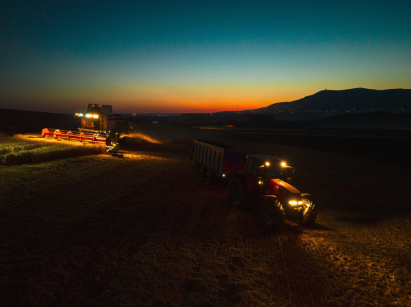 Aerial view of a tractor a harvester working on field during night. Agriculture and cultivation of industrial farms. Agribusiness.