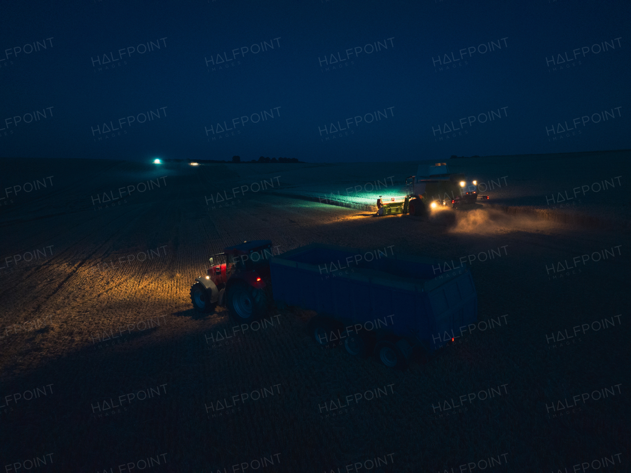 Aerial view of a tractor a harvester working on field during night. Agriculture and cultivation of industrial farms. Agribusiness.