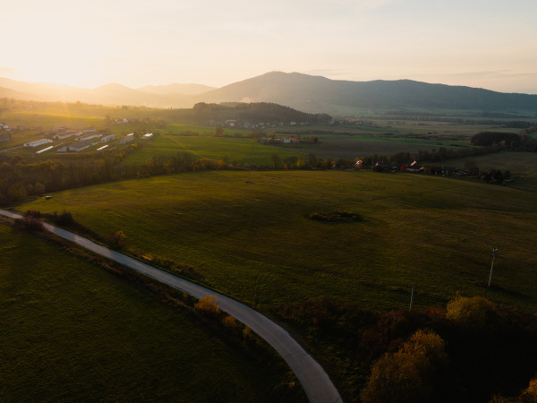 Aerial view of green summer farm fields, crops or pasture with road and mountains during sunset.