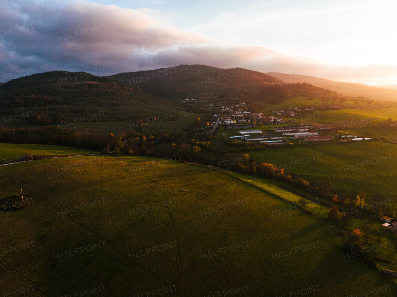 Aerial view of small farm village in the middle of green summer farm fields, crops or pasture with road and mountains.