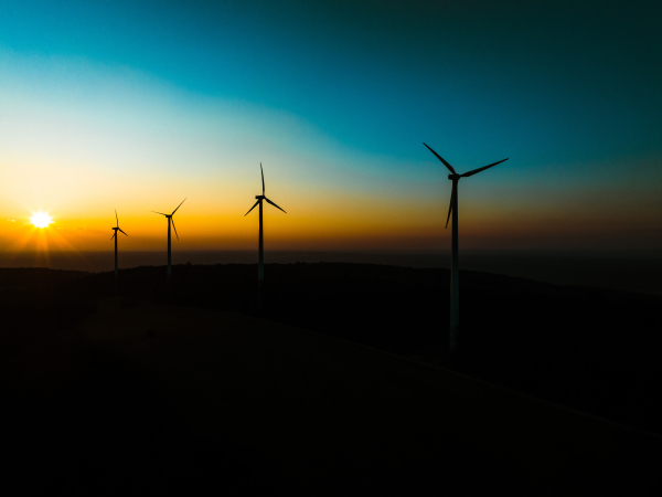 Aerial landscape photography of sunrise over nature with wind turbines. Wind turbine towers in soft morning light with forest, trees around, harmony of nature and technology. Concept of wind power as clean, renewable energy source.