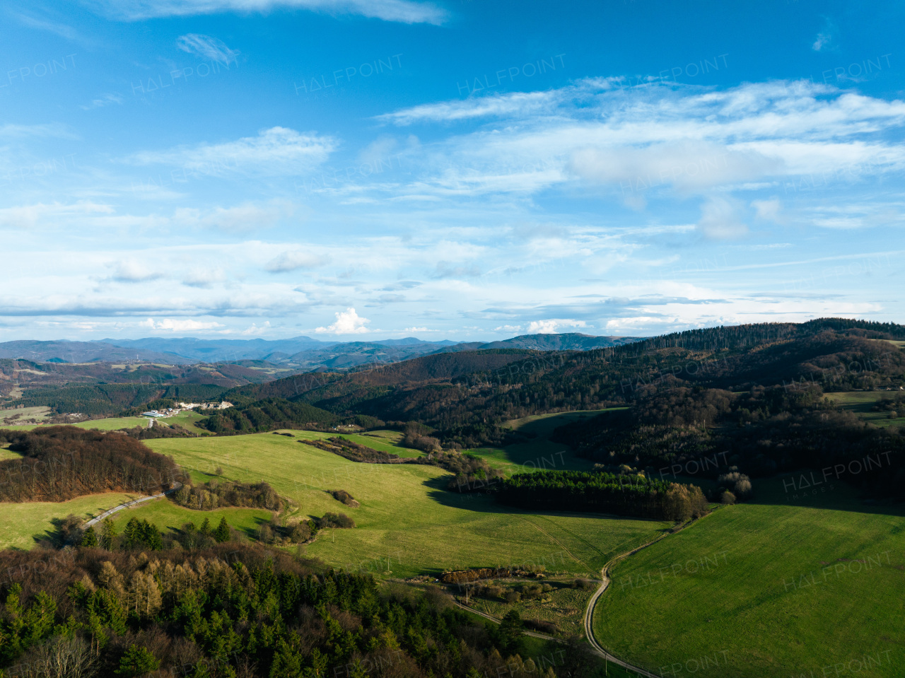 Aerial view of green summer farm fields, crops or pasture with road and mountains.