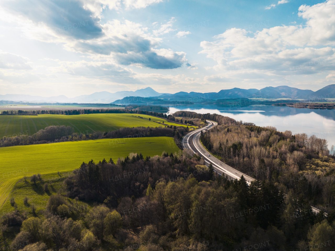 Aerial view of green summer nature with lake, crops or pasture with road and mountains.