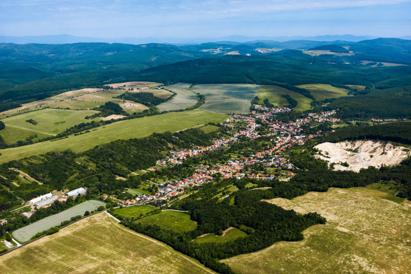 Aerial view of small village in the middle of green summer farm fields, crops or pasture with road and mountains.