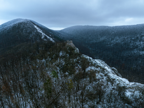 Aerial view of old ruins of fortress in the middle of winter forest. Drone view of snowy landscape with broken stone walls. Castle ruins.