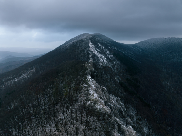 Aerial view of old ruins of fortress in the middle of winter forest. Drone view of snowy landscape with broken stone walls. Castle ruins.