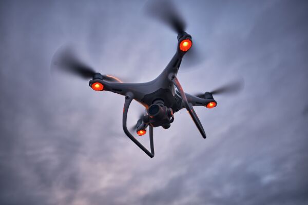 Aerial view of flying black drone, shot from below. Cloudy sky during sunset.