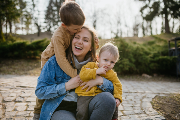 A happy young mother squatting and holding her little children, having fun, laughing in park in autumn.