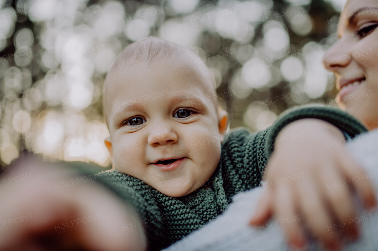 A close-up of mother holding her little baby son wearing knitted sweater during walk in nature.