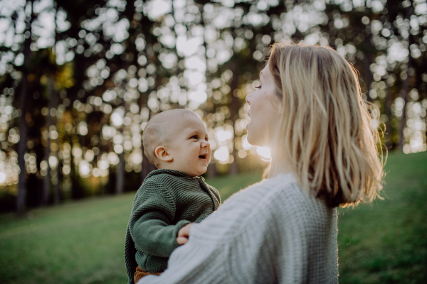 A mother holding her little baby son wearing knitted sweater during walk in nature, close-up