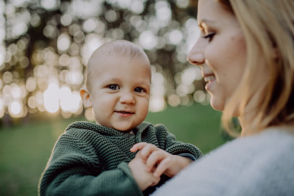 A mother holding her little baby son wearing knitted sweater during walk in nature, close-up