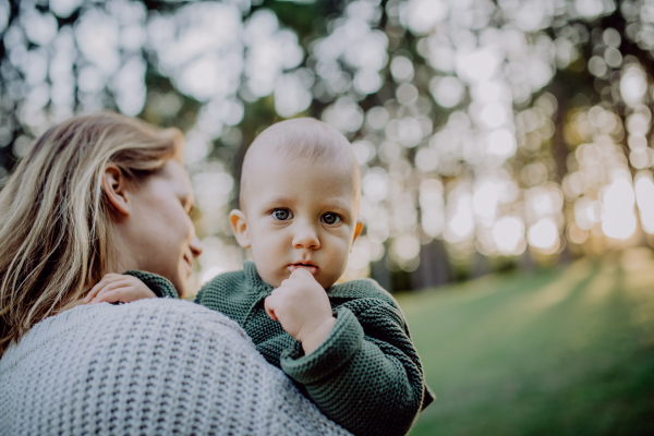 A mother holding her little baby son wearing knitted sweater during walk in nature, close-up