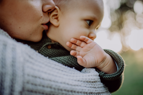 A mother holding her little baby son wearing knitted sweater during walk in nature, close-up