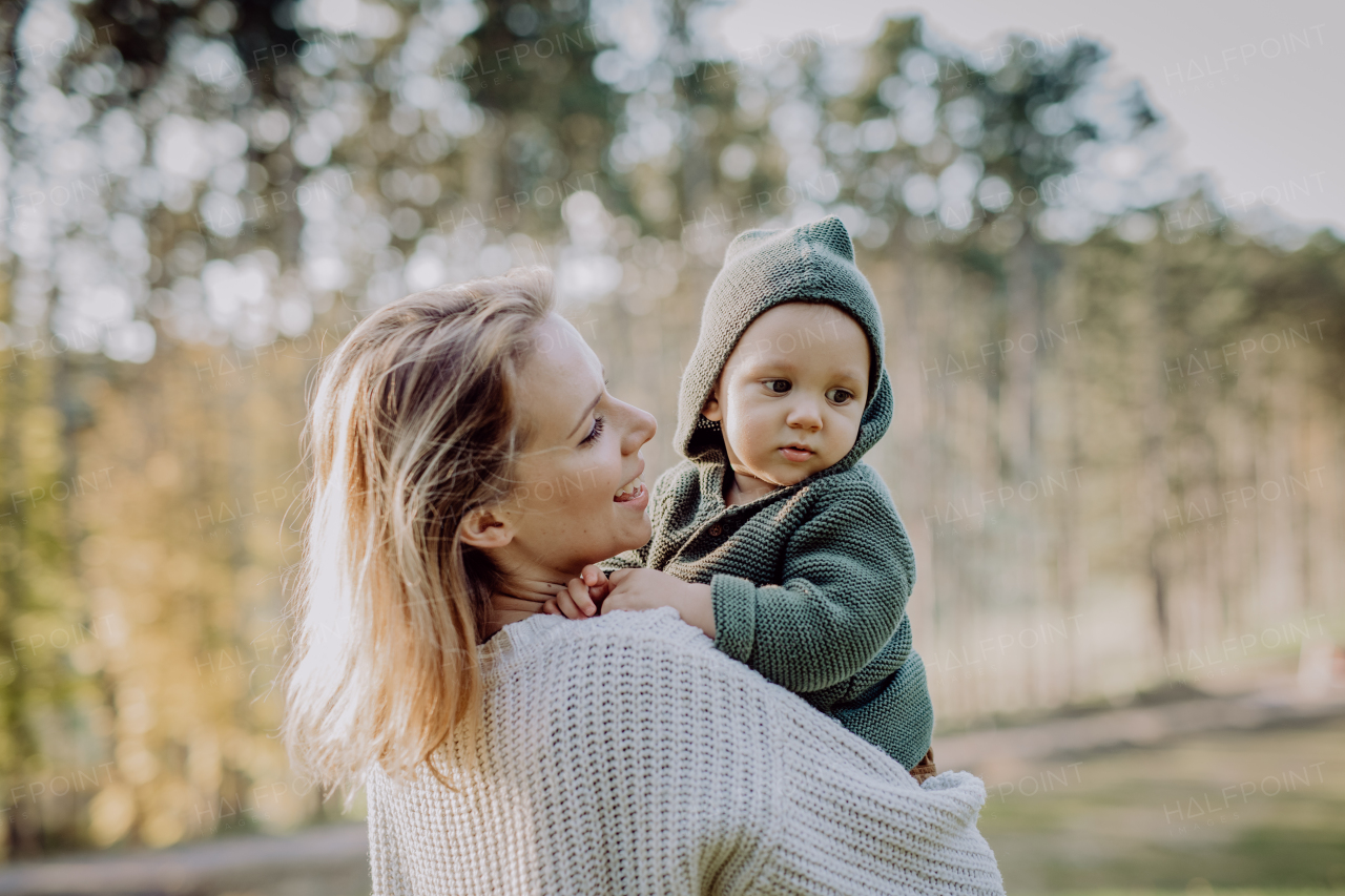 A mother holding her little baby son wearing knitted sweater during walk in nature.