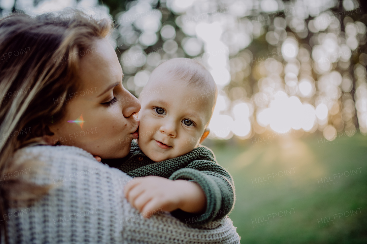 A mother holding her little baby son wearing knitted sweater during walk in nature.