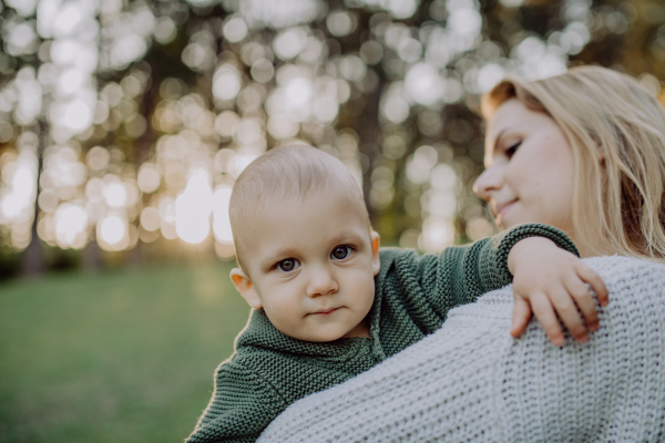 A mother holding her little baby son wearing knitted sweater during walk in nature.