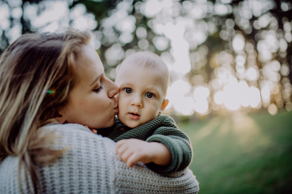 A mother holding her little baby son wearing knitted sweater during walk in nature.