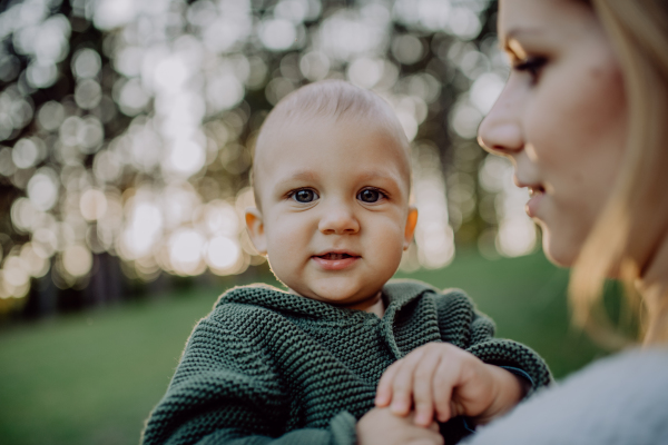 A mother holding her little baby son wearing knitted sweater during walk in nature.