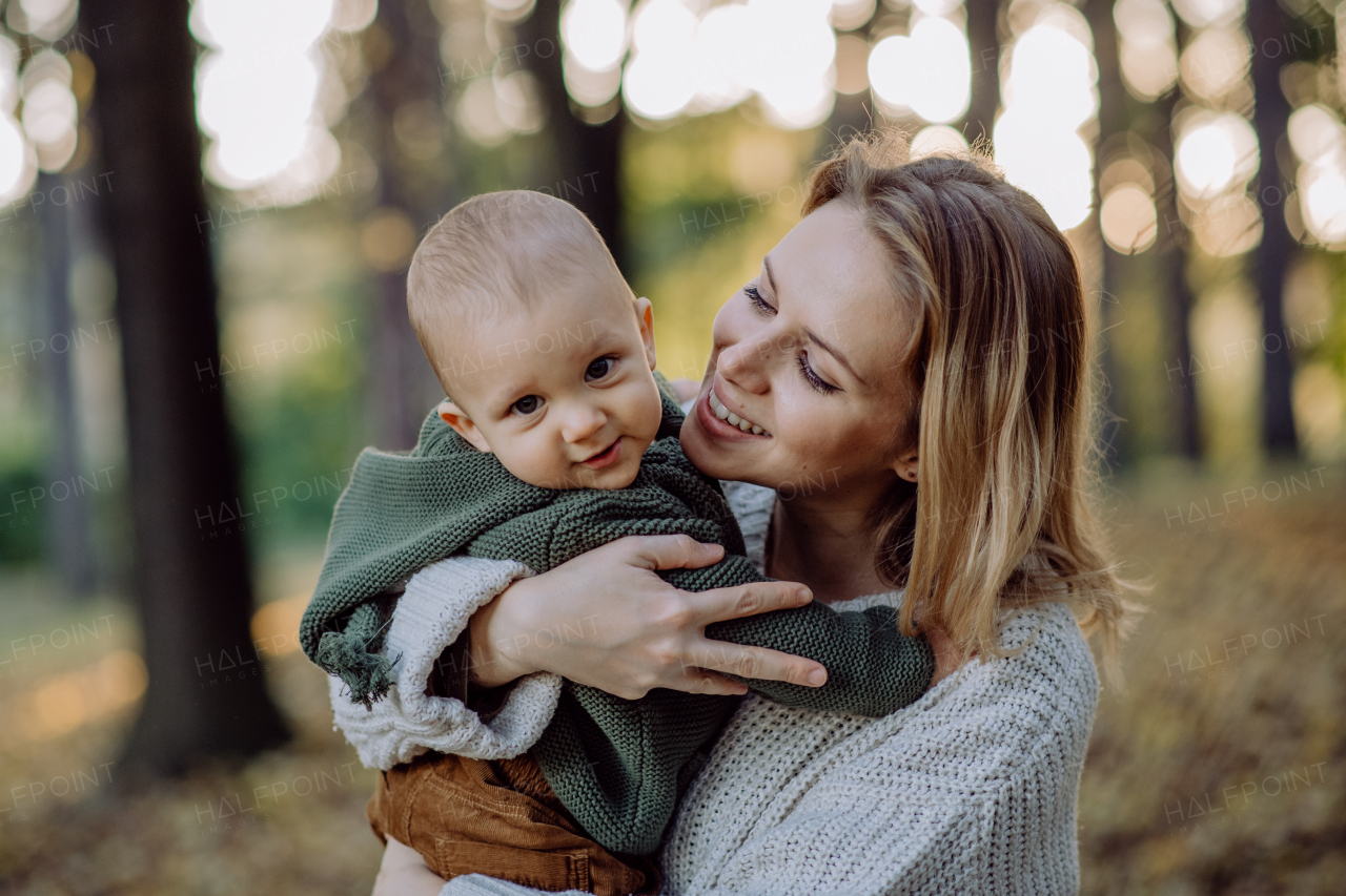 A mother holding her little baby son wearing knitted sweater during walk in nature.