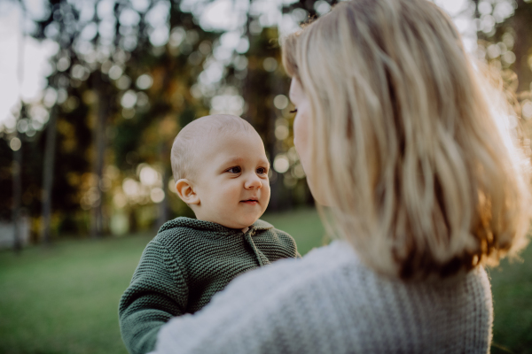 A mother holding her little baby son wearing knitted sweater during walk in nature.