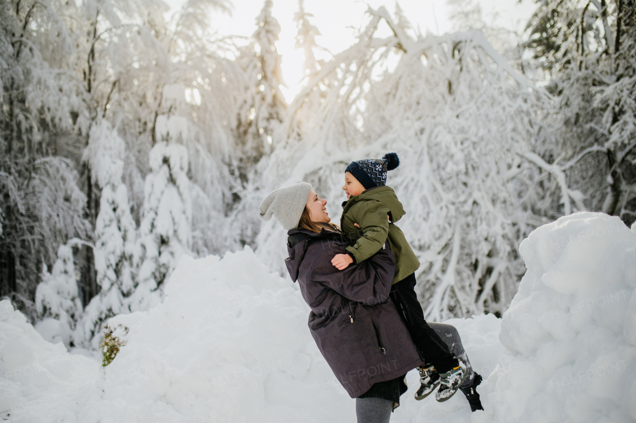 Mother holding her big son in the winter nature and enjoying snow.