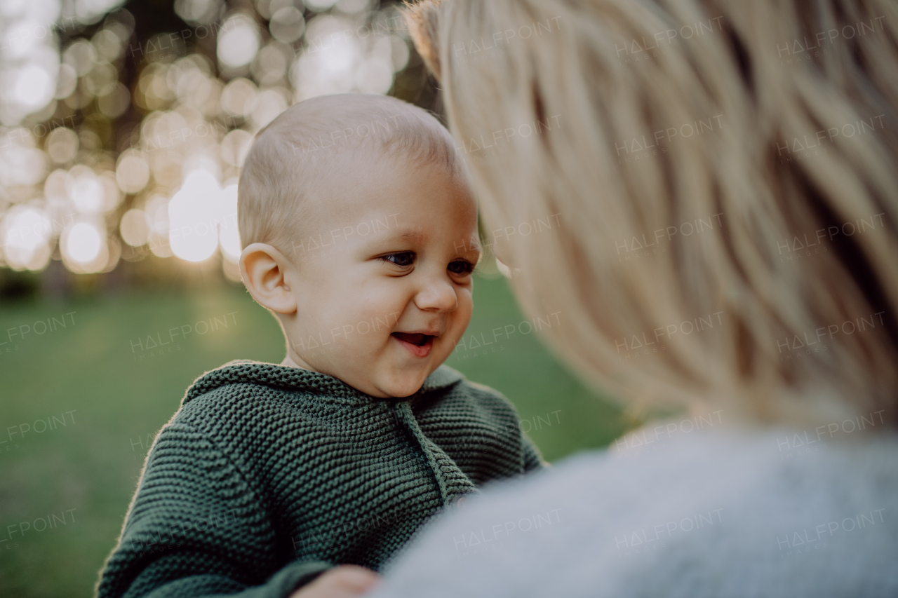 A mother holding her little baby son wearing knitted sweater during walk in nature, looking at camera.