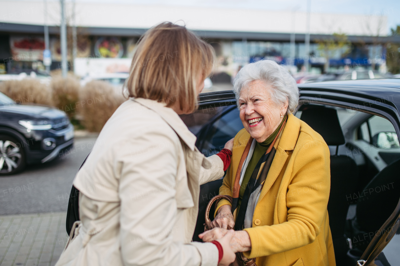 Senior lady getting out of the car, caregiver helping her, holding her hands. Elderly woman has problem with standing up from car back seat.