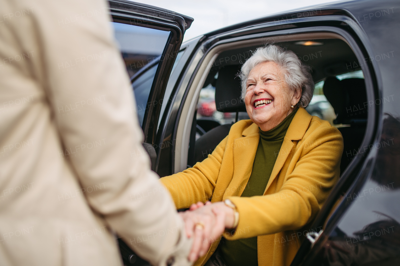 Senior lady getting out of the car, caregiver helping her, holding her hands. Elderly woman has problem with standing up from car back seat.