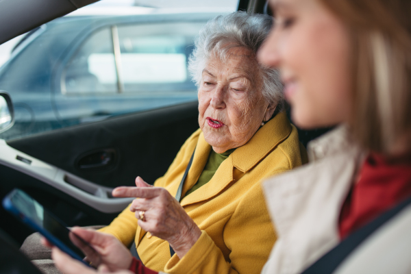 Granddaughter driving her elderly grandmother in the car, taking her to the doctor, shopping or to bank. Caregiver driving elderly lady to the church, pharmacy, searching for a route on a smartphone.