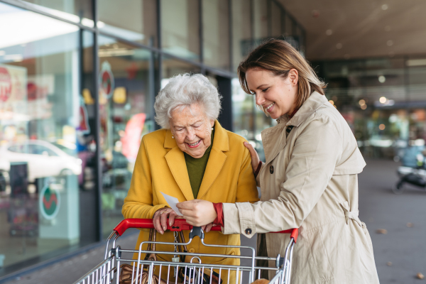 Mature daughter helping to check senior mother receipt after purchase, looking at amount of money spent, ensuring all charges are correct.