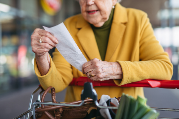 An elderly woman checking her receipt after a purchase, looking at the amount of money spent, ensuring all charges are correct.