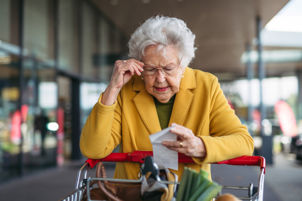 An elderly woman checking her receipt after a purchase, looking at the amount of money spent, ensuring all charges are correct.