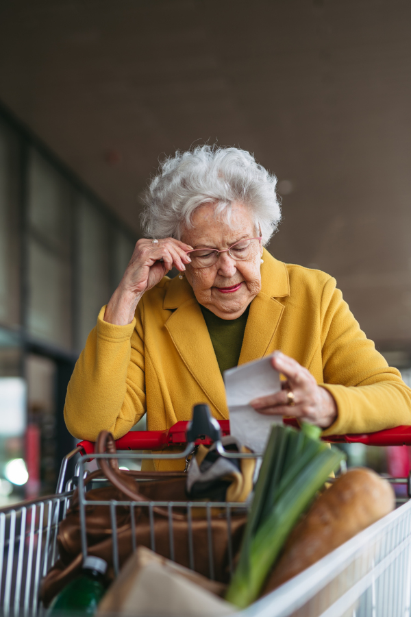 An elderly woman checking her receipt after a purchase, looking at the amount of money spent, ensuring all charges are correct.