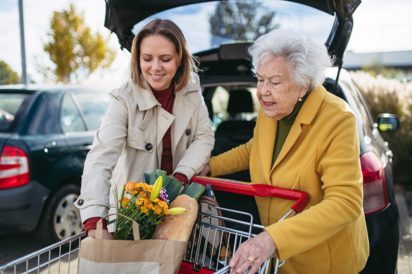 Mature granddaughter helping her grandmother load groceries in to the car. Senior woman shopping at the shopping center.