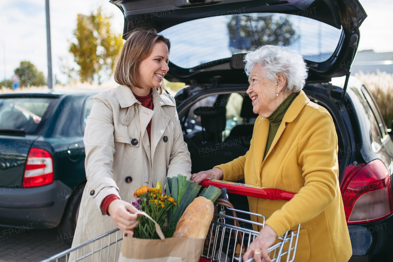 Mature granddaughter helping her grandmother load groceries in to the car. Senior woman shopping at the shopping center.