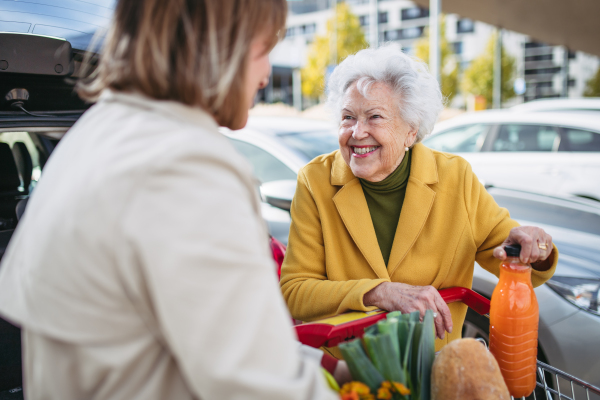 Mature granddaughter helping her grandmother load groceries in to the car. Senior woman shopping at the shopping center.