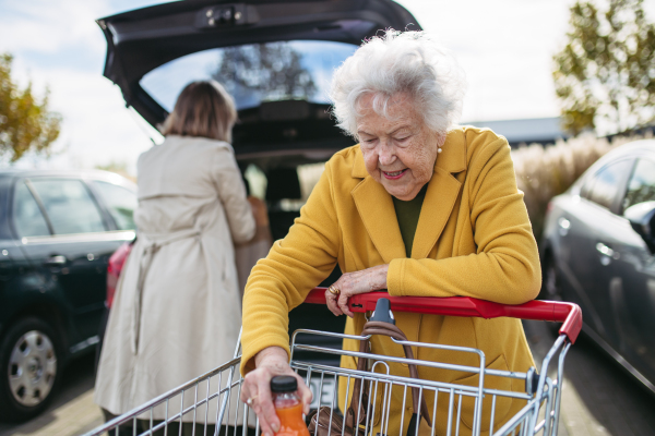 Mature granddaughter helping her grandmother load groceries in to the car. Senior woman shopping at the shopping center.