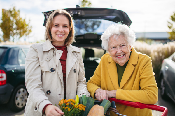 Mature granddaughter helping her grandmother load groceries in to the car. Senior woman shopping at the shopping center.