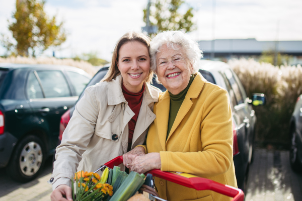 Mature granddaughter helping her grandmother load groceries in to the car. Senior woman shopping at the shopping center.