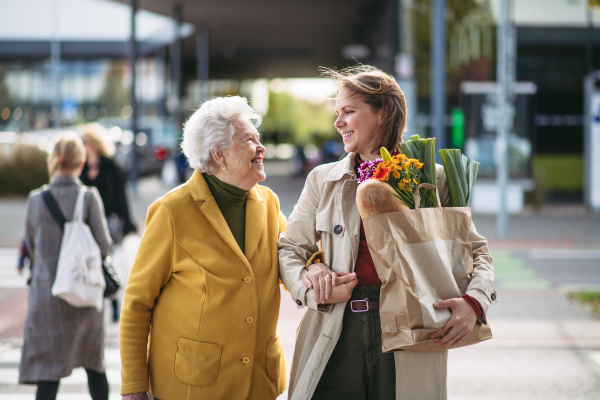 Mature granddaughter carrying groceries out to her grandmother's car. Senior woman shopping at the shopping center, needing help loading groceries into the car.