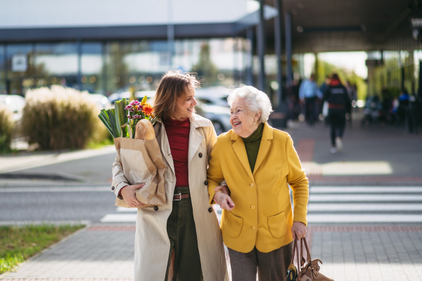 Mature granddaughter carrying groceries out to her grandmother's car. Senior woman shopping at the shopping center, needing help loading groceries into the car.