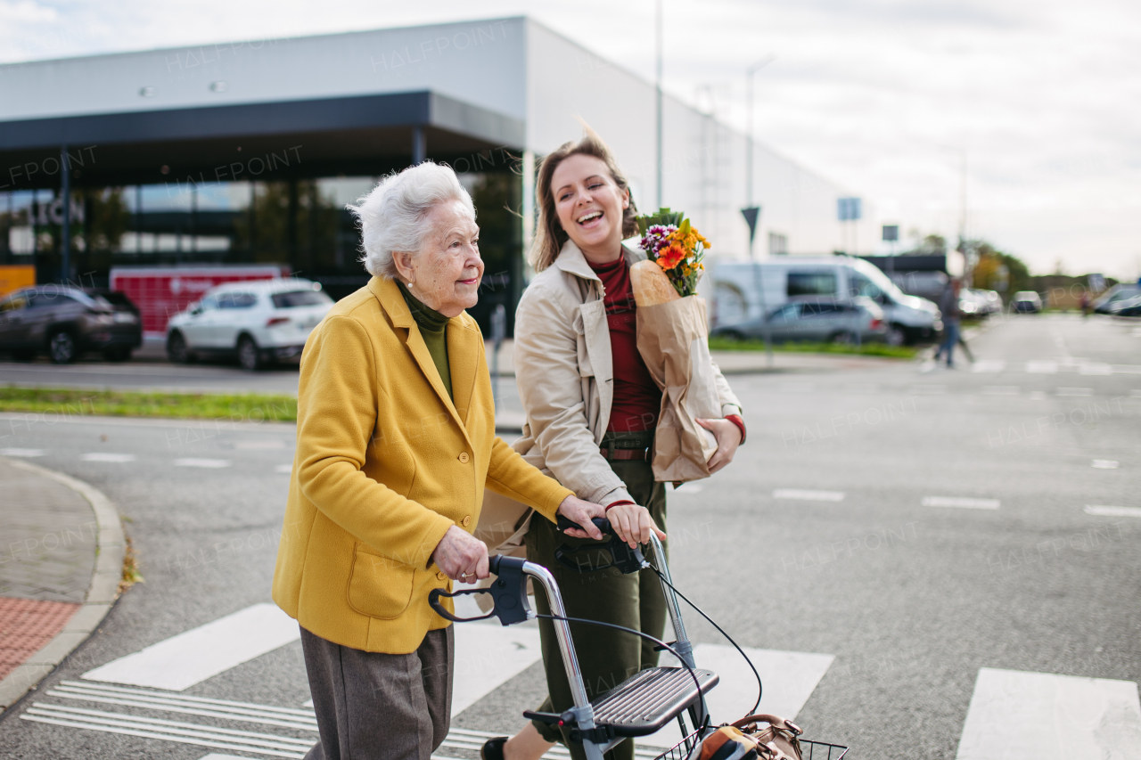 Mature granddaughter carrying grandmother's shopping bag. Senior woman and caregiver going to home with goceries from the supermarket, during cold autumn day.