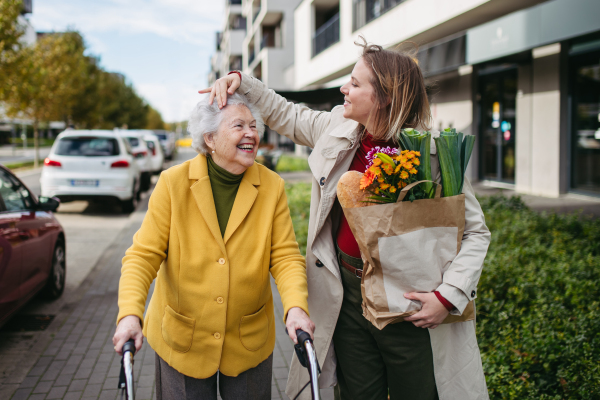 Mature granddaughter carrying grandmother's shopping bag. Senior woman and caregiver going to home with goceries from the supermarket, during cold autumn day.