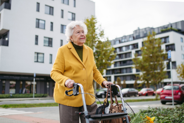 A senior woman with a mobility walker walking on the city streets during autumn day, enjoying the beautiful sunny weather. Elderly lady savoring every moment, living life to fullest.