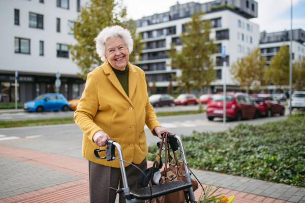 A senior woman with a mobility walker walking on the city streets during autumn day, enjoying the beautiful sunny weather. Elderly lady savoring every moment, living life to fullest.