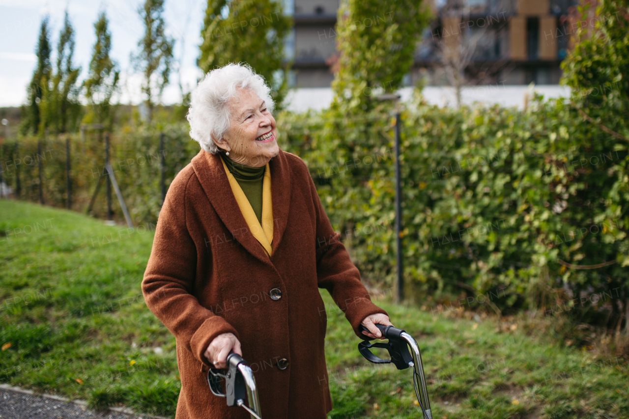 A senior woman with a mobility walker walking on the city streets during autumn day, enjoying the beautiful sunny weather. Elderly lady savoring every moment, living life to fullest.