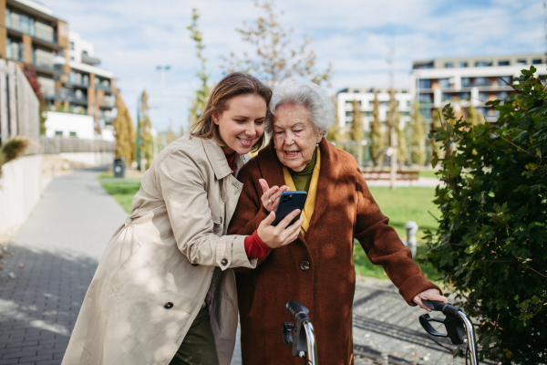 Mature granddaughter teaching grandmother how to use smartphone. Caregiver helping senior lady shopping online on her smartphone.