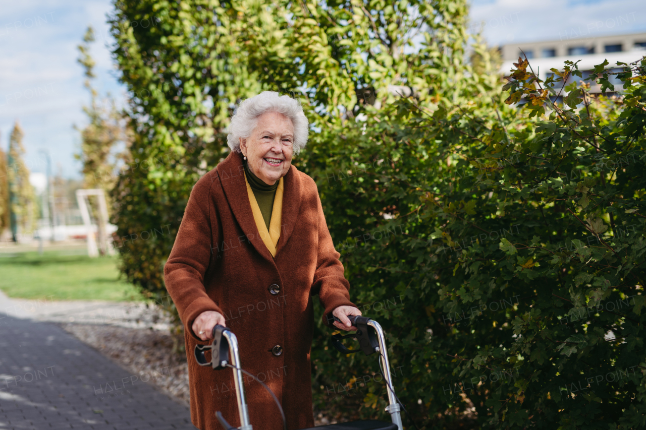 A senior woman with a mobility walker walking on the city streets during autumn day, enjoying the beautiful sunny weather. Elderly lady savoring every moment, living life to fullest.